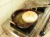 A puri floats in oil, which fills a rounded pot on a stove.